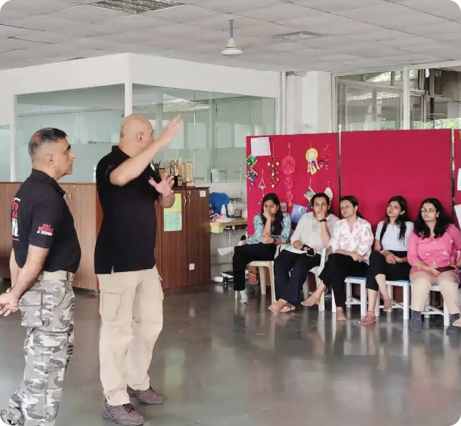 Self-defence training session where instructors demonstrate techniques to a group of women seated in a classroom setting